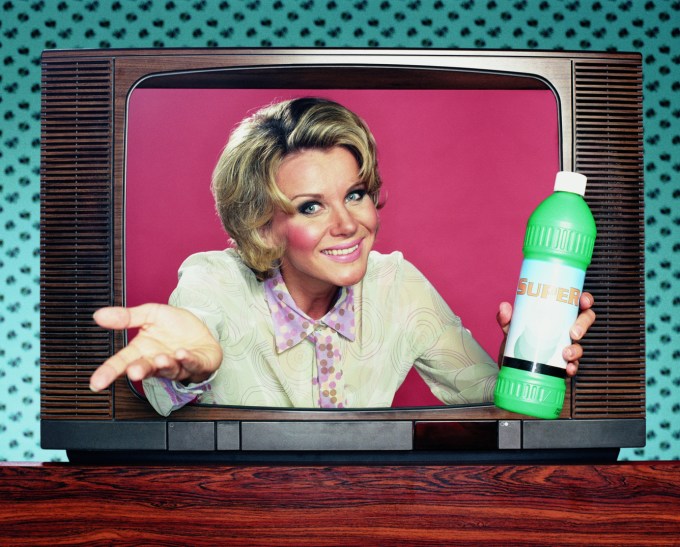 Woman holding domestic product emerging from television, portrait